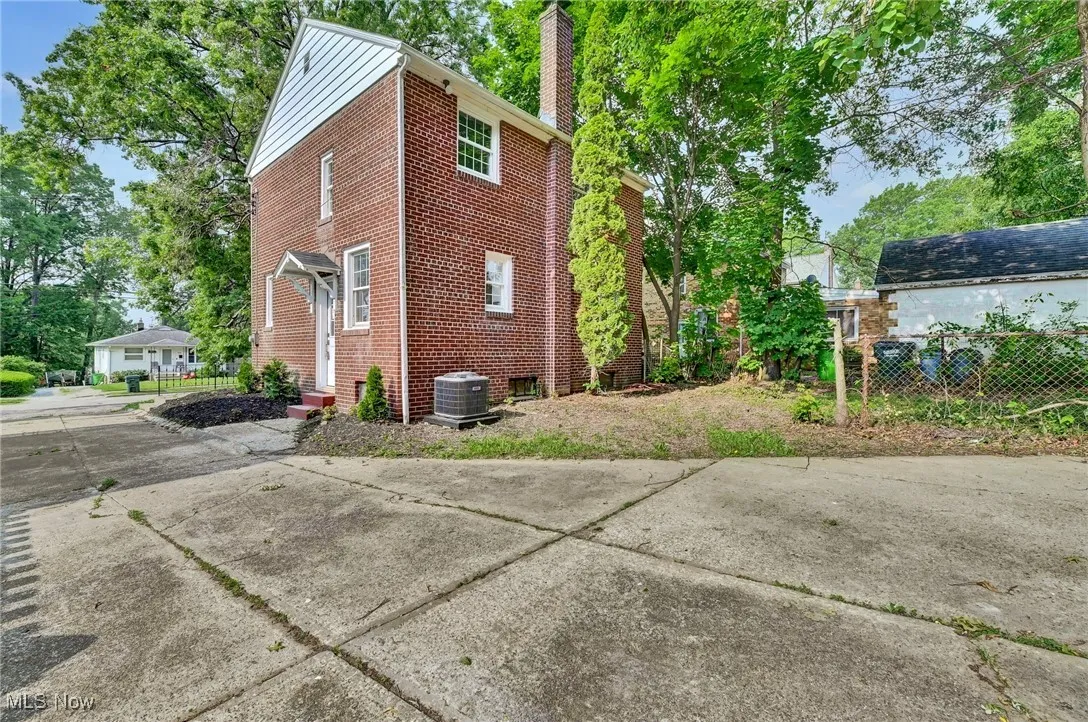 View of side of home with a chimney, brick siding, and cooling unit