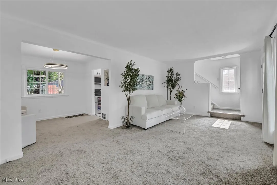 Living area with carpet, stairway, baseboards, a chandelier, and arched walkways