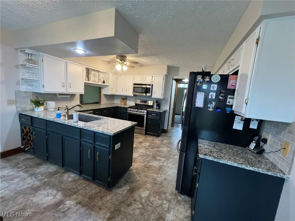 Kitchen with stainless steel appliances, a peninsula, a sink, a textured ceiling, and tasteful backsplash