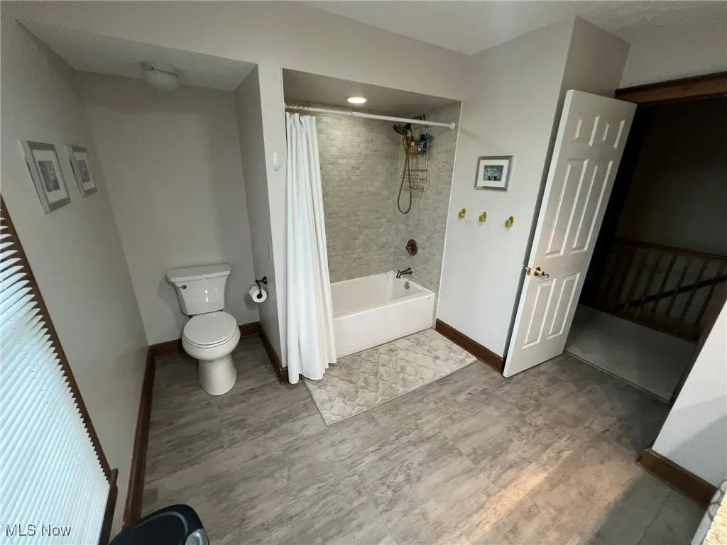 Full bathroom with wood finished floors, toilet, baseboards, and shower / bathtub combination with curtain