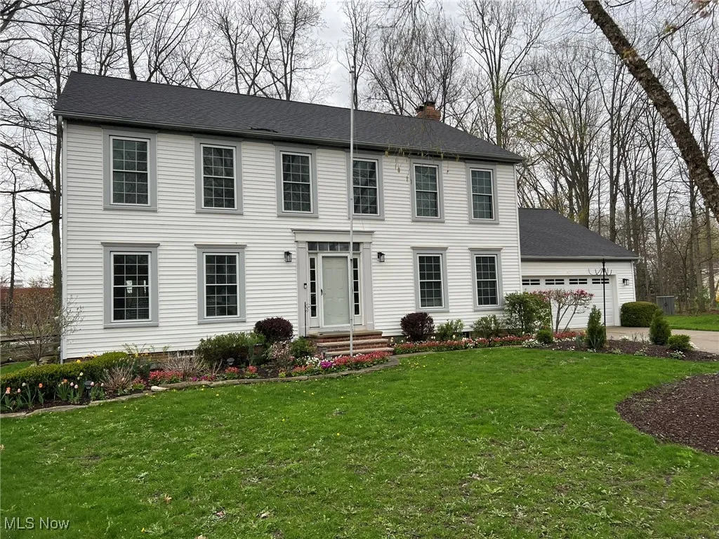 Colonial home featuring a shingled roof, a chimney, a front yard, and concrete driveway