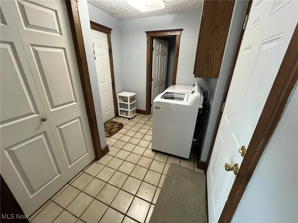 Washroom with baseboards, light tile patterned flooring, a textured ceiling, and cabinet space