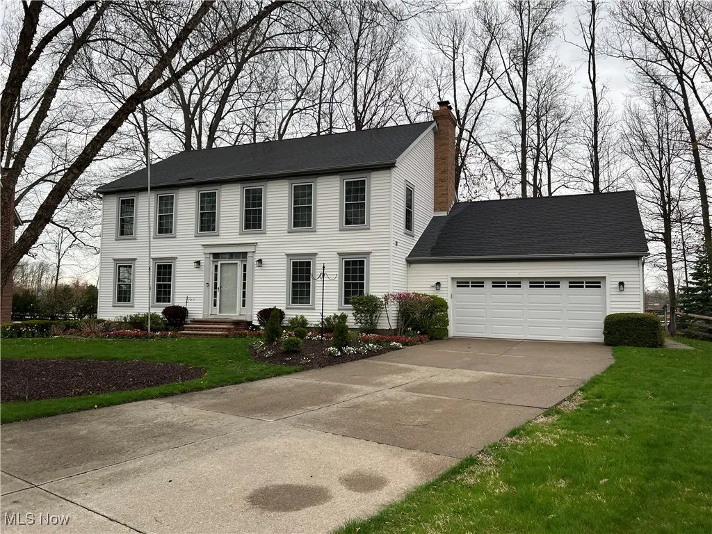Colonial house with an attached garage, a front lawn, a chimney, and concrete driveway