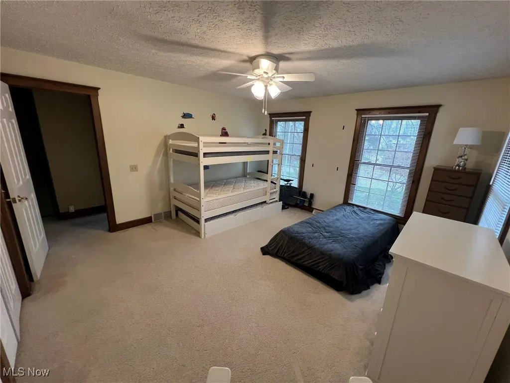 Bedroom featuring a ceiling fan, baseboards, a textured ceiling, and light colored carpet