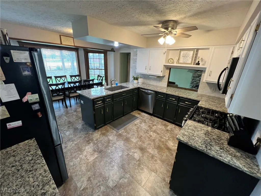 Kitchen with stainless steel dishwasher, dark cabinetry, a sink, freestanding refrigerator, and a textured ceiling