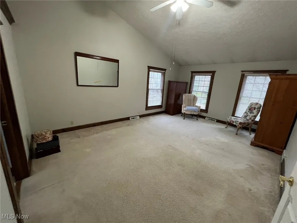 Unfurnished room with a textured ceiling, baseboards, light colored carpet, lofted ceiling, and a ceiling fan