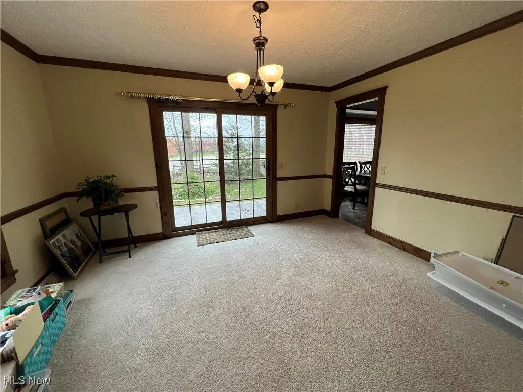 Carpeted spare room featuring crown molding, an inviting chandelier, a healthy amount of sunlight, and a textured ceiling