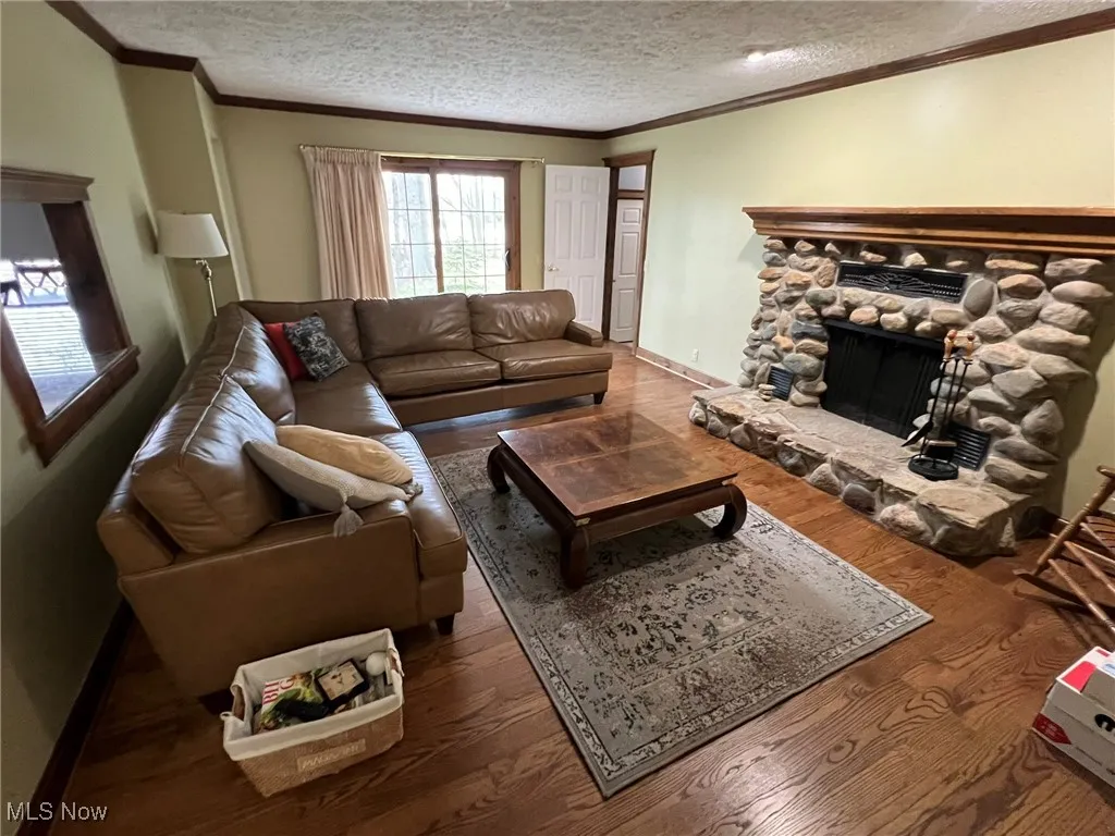 Living room with wood finished floors, a stone fireplace, a textured ceiling, and ornamental molding