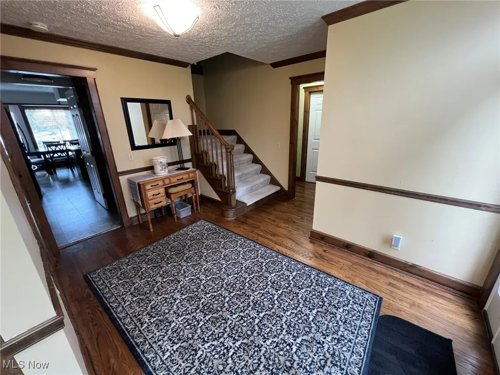 Entryway with crown molding, stairs, wood finished floors, a textured ceiling, and baseboards