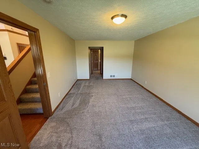 Spare room featuring a textured ceiling, carpet, visible vents, and baseboards