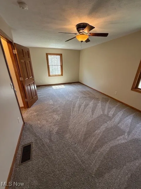 Spare room with visible vents, carpet flooring, baseboards, and a ceiling fan