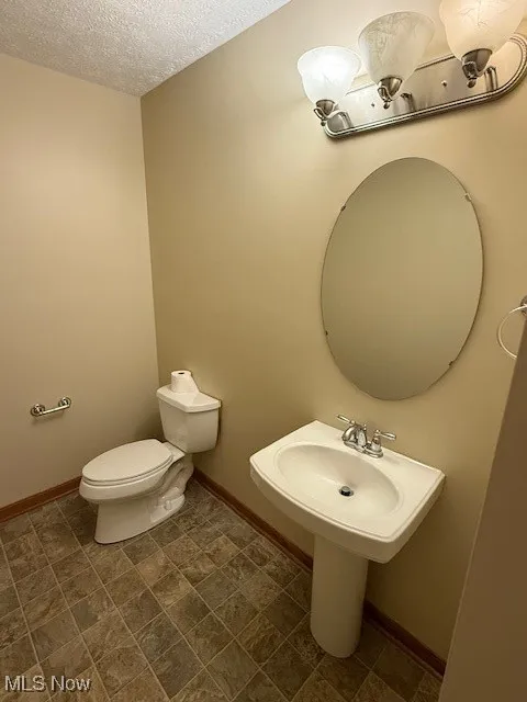 Bathroom featuring a textured ceiling, toilet, baseboards, and a sink