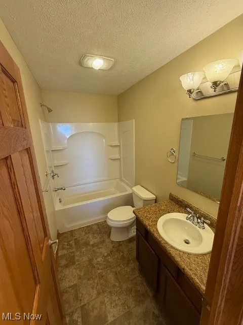 Bathroom with tub / shower combination, a textured ceiling, toilet, and vanity