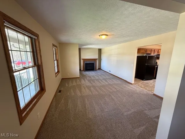 Unfurnished living room featuring visible vents, light carpet, baseboards, a fireplace, and a textured ceiling