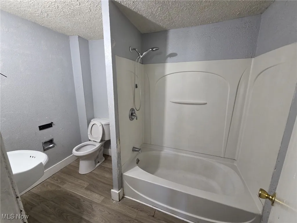 Bathroom featuring bathing tub / shower combination, a textured ceiling, toilet, wood finished floors, and a textured wall