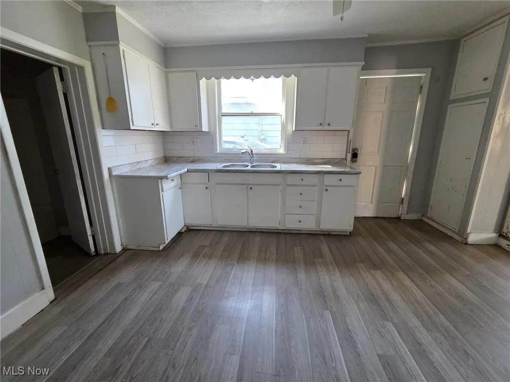 Kitchen with dark wood-style floors, light countertops, a sink, decorative backsplash, and white cabinetry