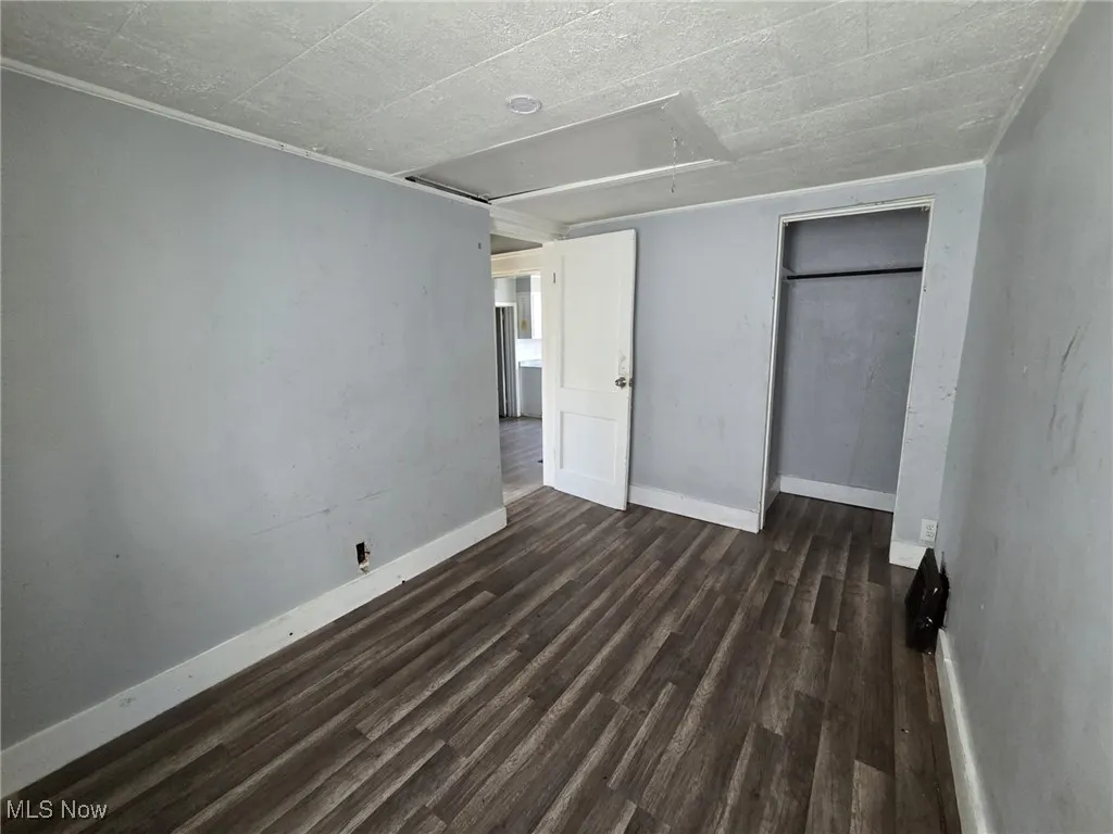 Unfurnished bedroom with attic access, baseboards, dark wood-type flooring, and a closet