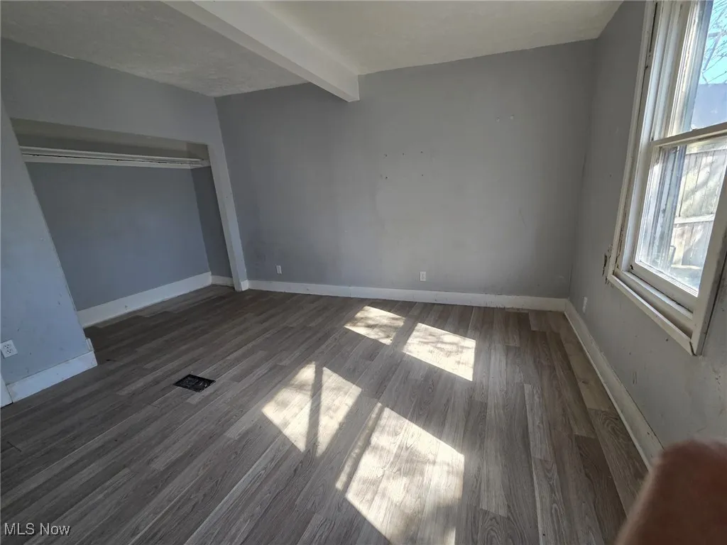 Unfurnished bedroom featuring beamed ceiling, wood finished floors, and multiple windows