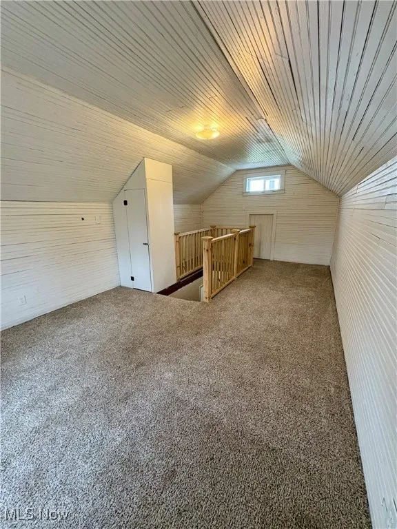 Additional living space featuring wooden walls, vaulted ceiling, and carpet flooring