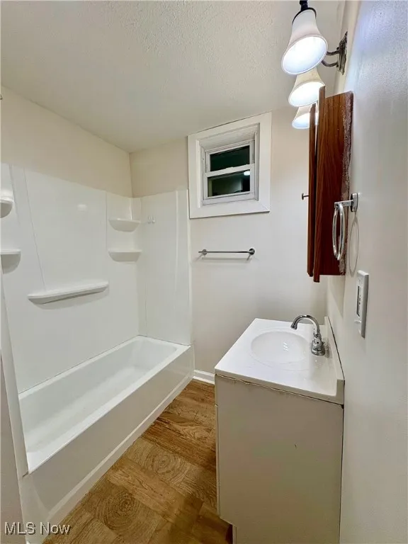 Full bathroom featuring baseboards, wood finished floors, a textured ceiling, and vanity