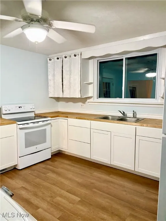 Kitchen featuring light wood finished floors, a sink, butcher block countertops, white cabinetry, and white range with electric cooktop