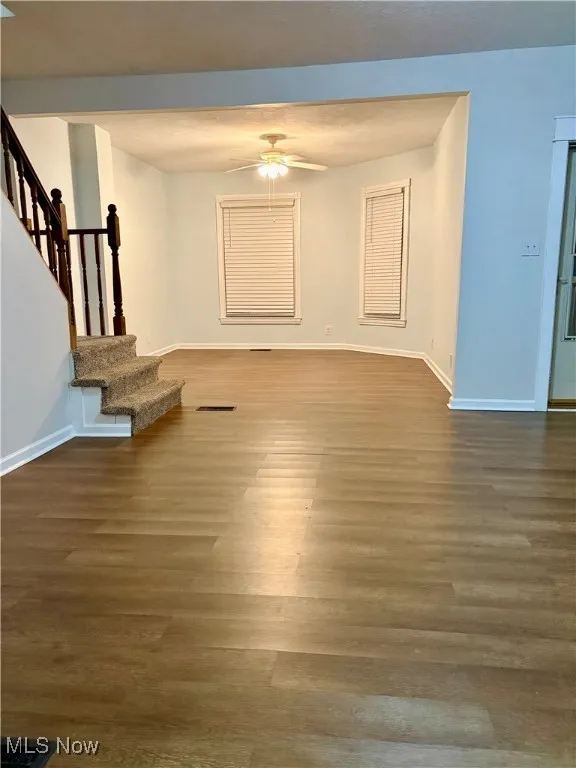 Unfurnished living room featuring wood finished floors, stairs, a ceiling fan, and baseboards