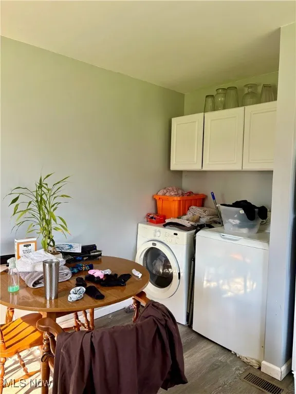 Laundry area with washing machine and clothes dryer, dark wood-style flooring, visible vents, and cabinet space
