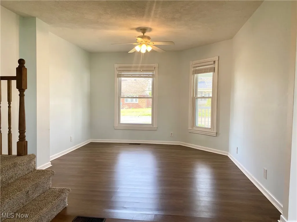 Unfurnished living room featuring stairway, a textured ceiling, ceiling fan, dark wood finished floors, and baseboards
