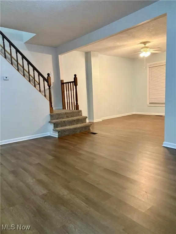 Unfurnished living room featuring baseboards, wood finished floors, stairs, and ceiling fan