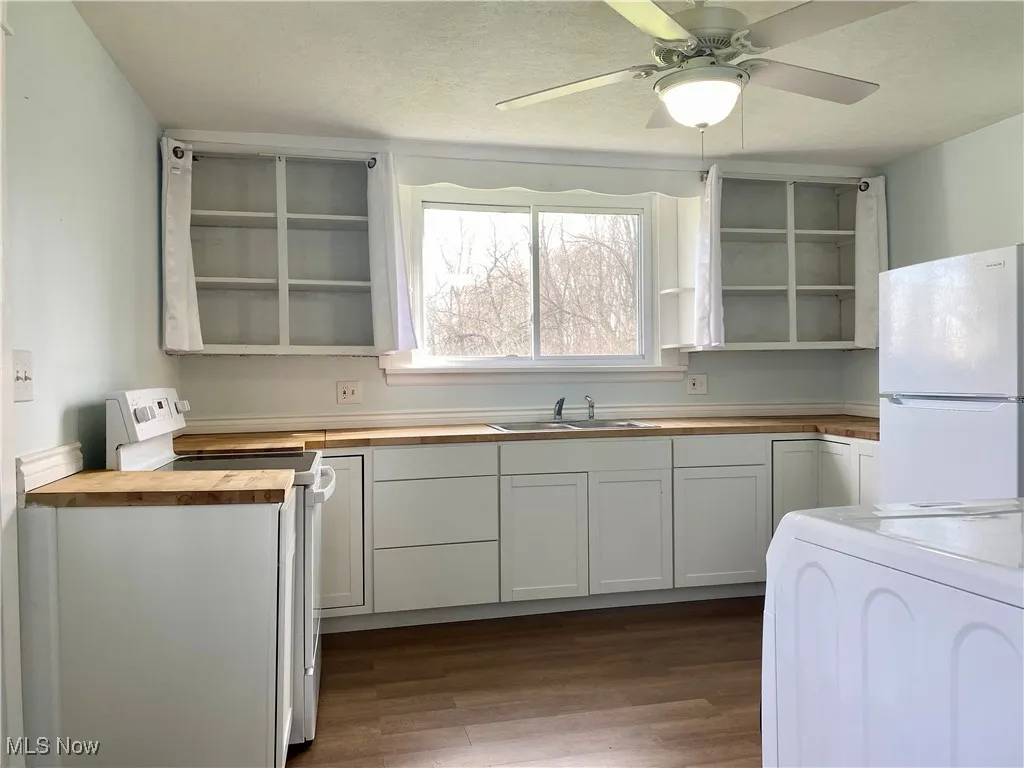 Kitchen featuring a sink, dark wood-style flooring, butcher block countertops, white appliances, and open shelves