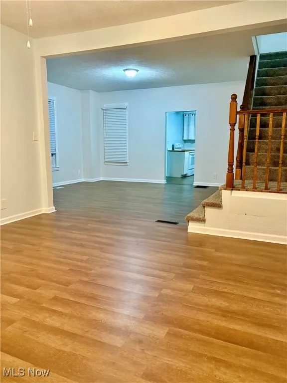 Unfurnished living room featuring visible vents, baseboards, wood finished floors, and stairs