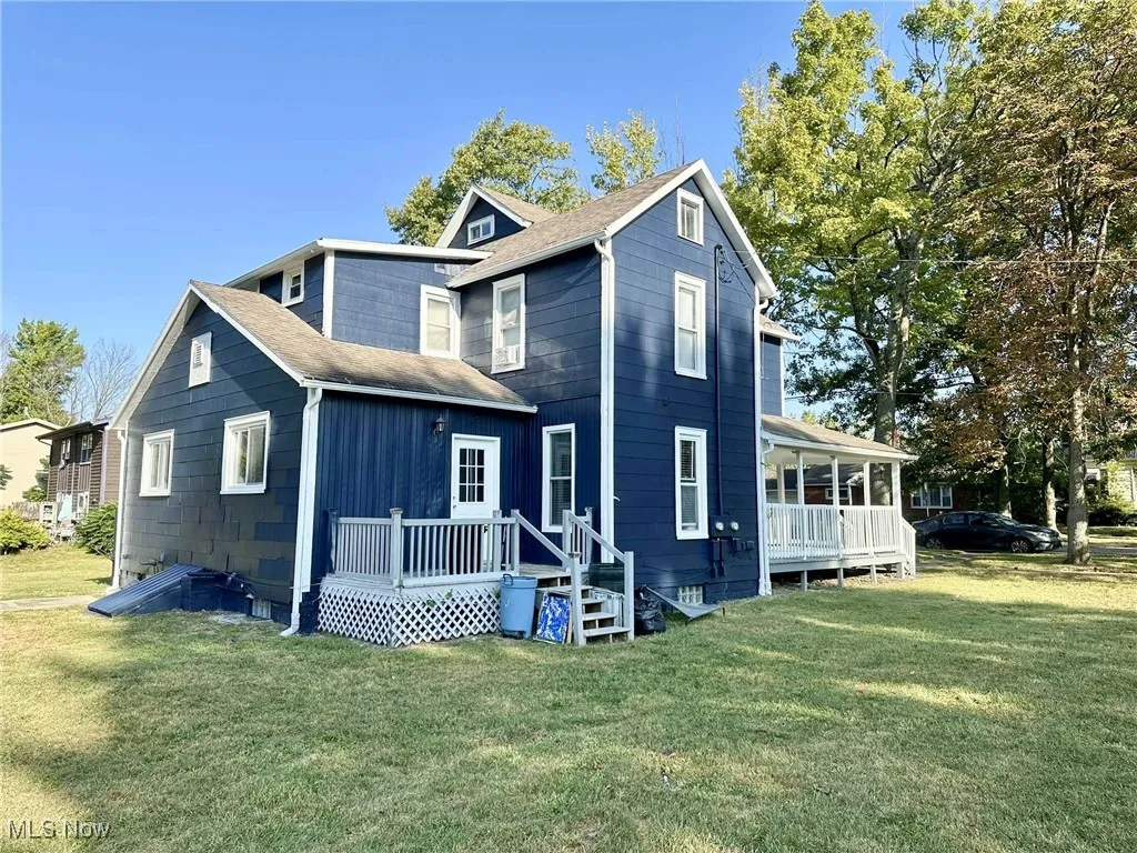 View of front facade with roof with shingles, a deck, and a front yard
