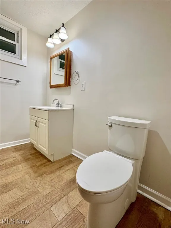 Half bathroom featuring a textured ceiling, toilet, baseboards, wood finished floors, and vanity