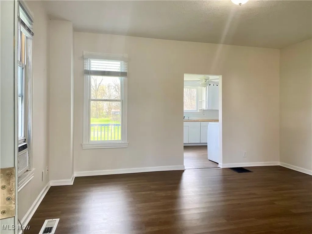 Unfurnished room featuring baseboards, visible vents, a wealth of natural light, and dark wood-style flooring