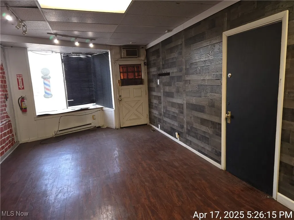 Unfurnished room with dark wood finished floors, track lighting, wood walls, and baseboards