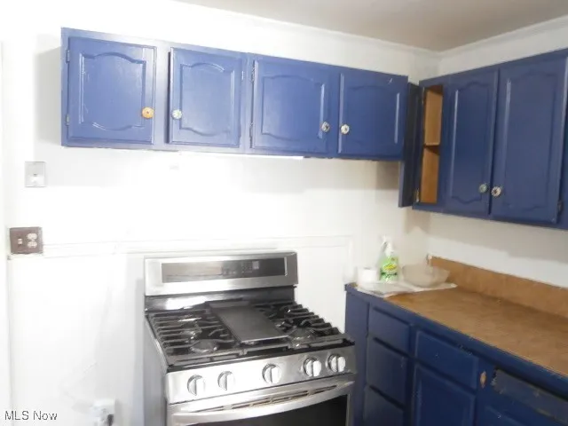 Kitchen with blue cabinets, stainless steel range with gas cooktop, and dark countertops