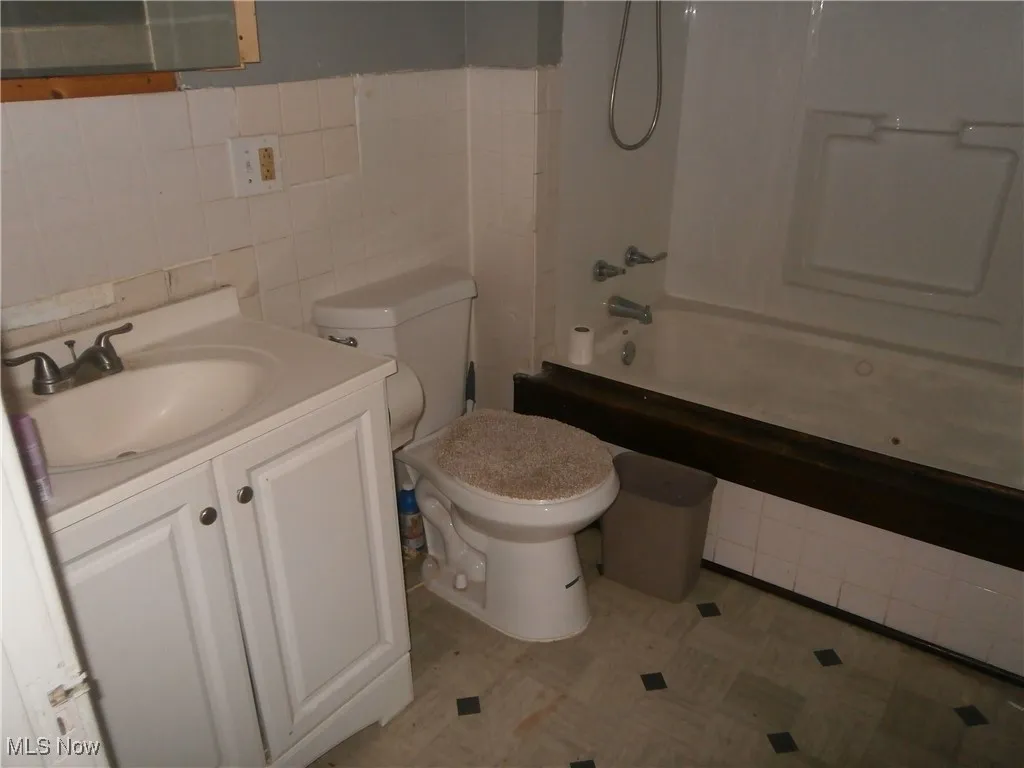 Bathroom featuring tile patterned floors, toilet, vanity, tile walls, and  shower combination