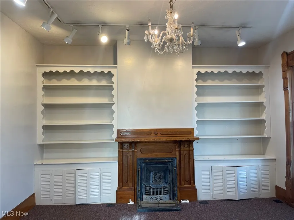 Unfurnished living room with carpet flooring, baseboards, an inviting chandelier, track lighting, and a fireplace