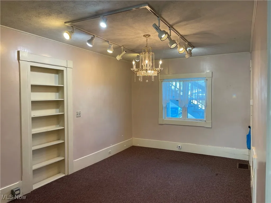 Spare room with track lighting, dark carpet, baseboards, a notable chandelier, and visible vents