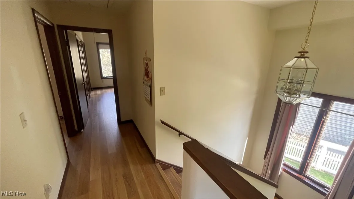 Hall with a notable chandelier, baseboards, a healthy amount of sunlight, and wood finished floors