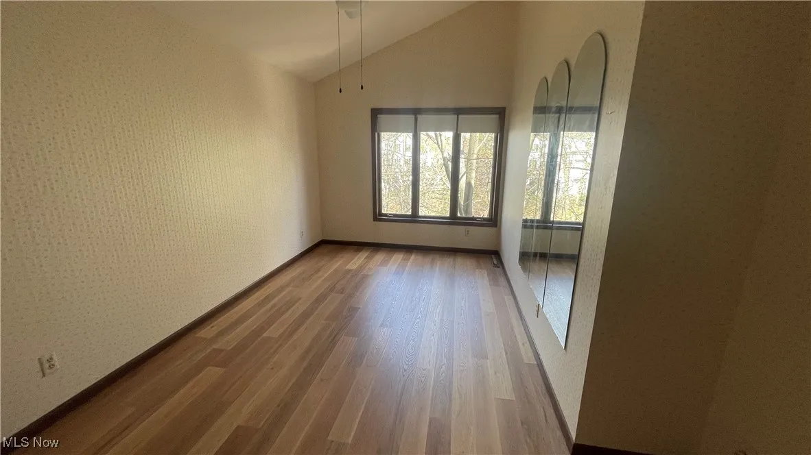Unfurnished room featuring lofted ceiling, baseboards, and wood finished floors