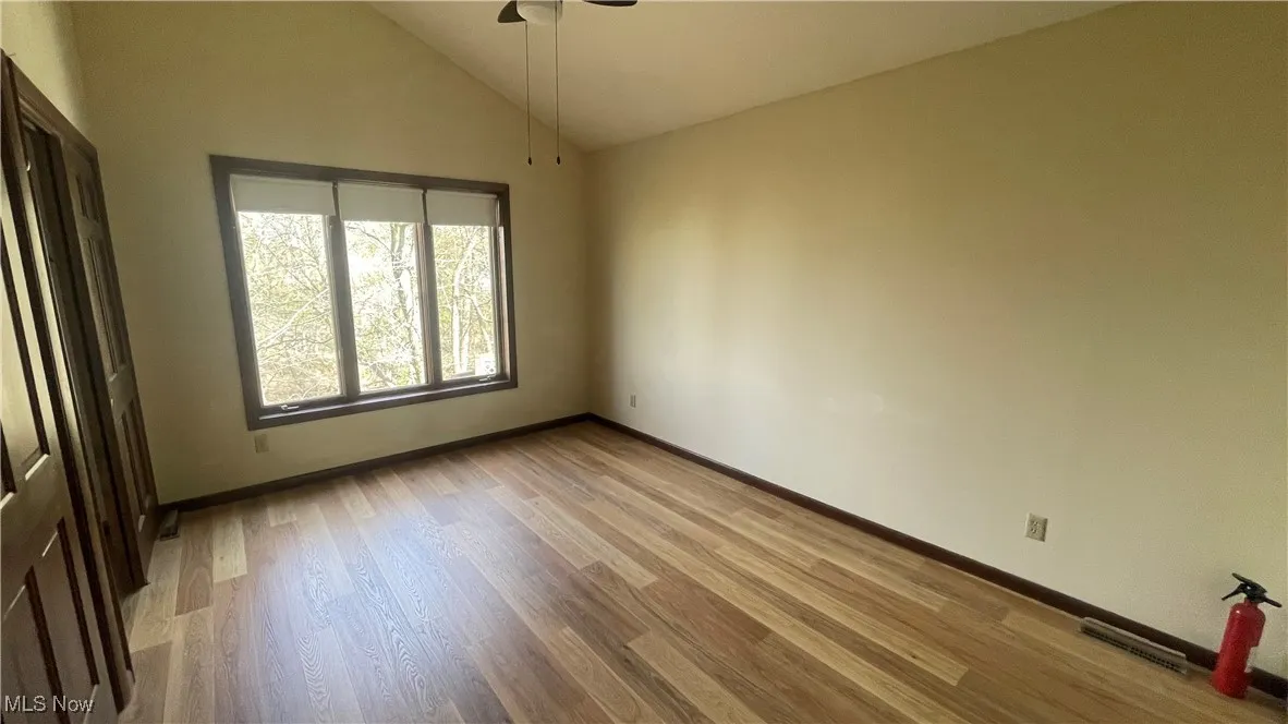 Unfurnished room featuring visible vents, baseboards, a ceiling fan, wood finished floors, and high vaulted ceiling