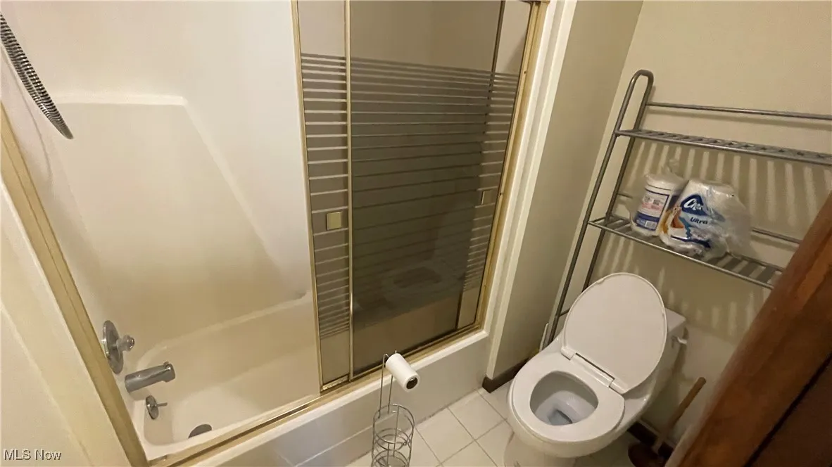 Full bathroom with tile patterned flooring, bath / shower combo with glass door, and toilet