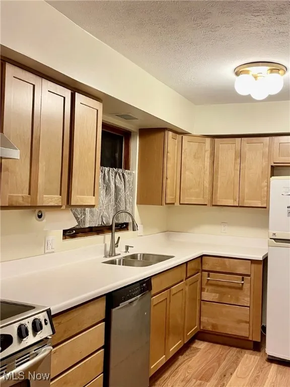 Kitchen featuring a textured ceiling, a sink, stainless steel appliances, light wood finished floors, and light countertops