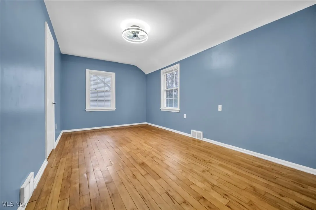 Unfurnished room featuring hardwood / wood-style flooring, lofted ceiling, visible vents, and baseboards