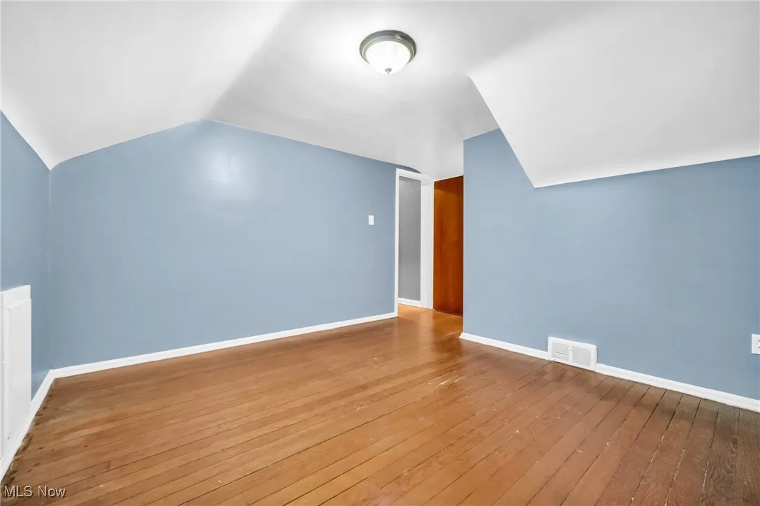 Additional living space with wood-type flooring, vaulted ceiling, visible vents, and baseboards
