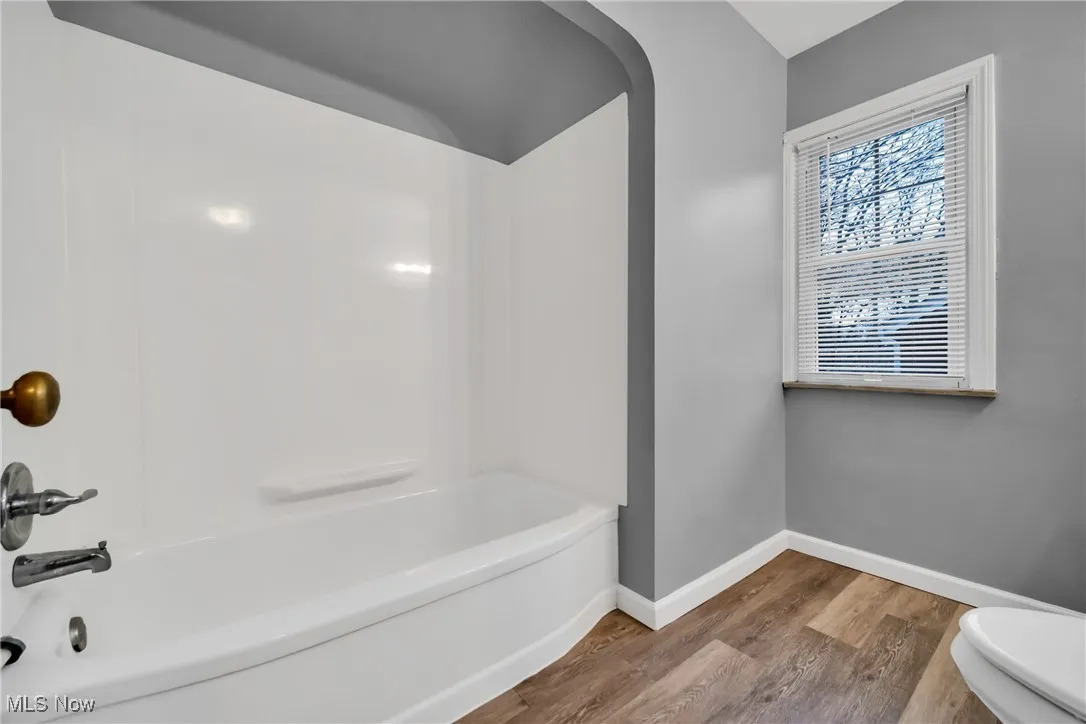 Bathroom featuring toilet, baseboards, bathtub / shower combination, and wood finished floors