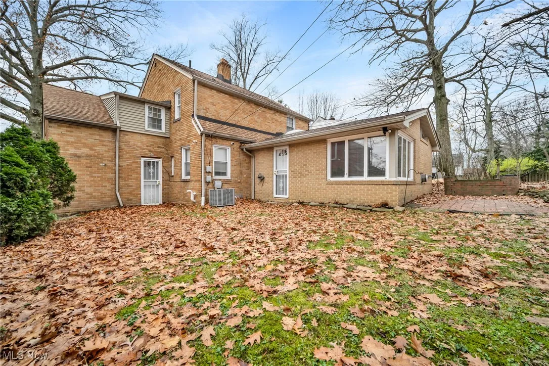 Rear view of house with central AC, brick siding, fence, and a chimney