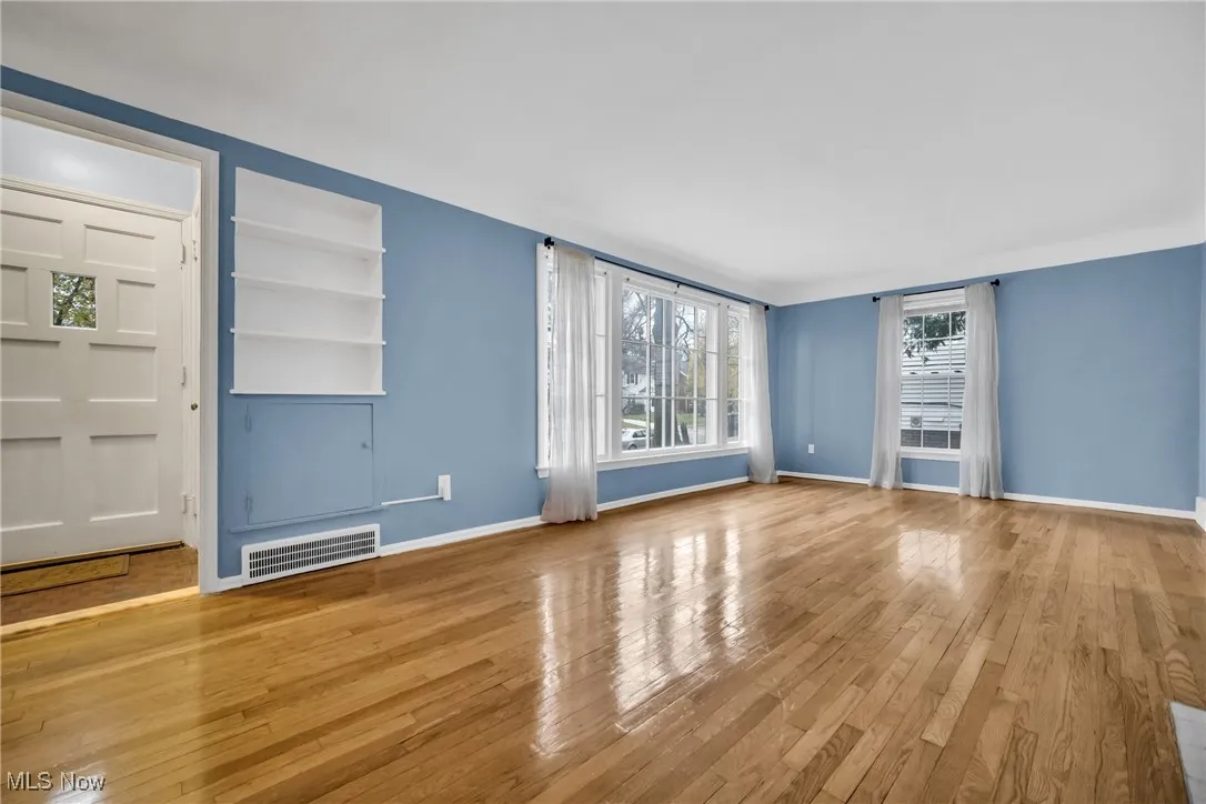 Unfurnished living room with baseboards, visible vents, built in features, and wood-type flooring