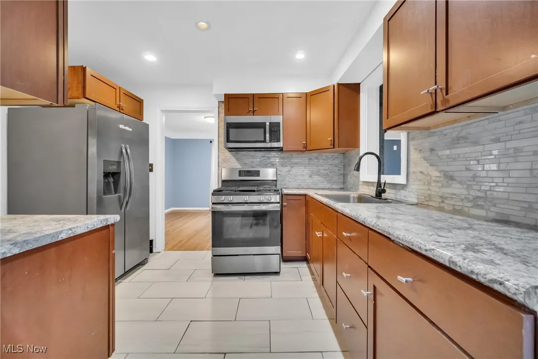 Kitchen featuring brown cabinets, backsplash, appliances with stainless steel finishes, and a sink